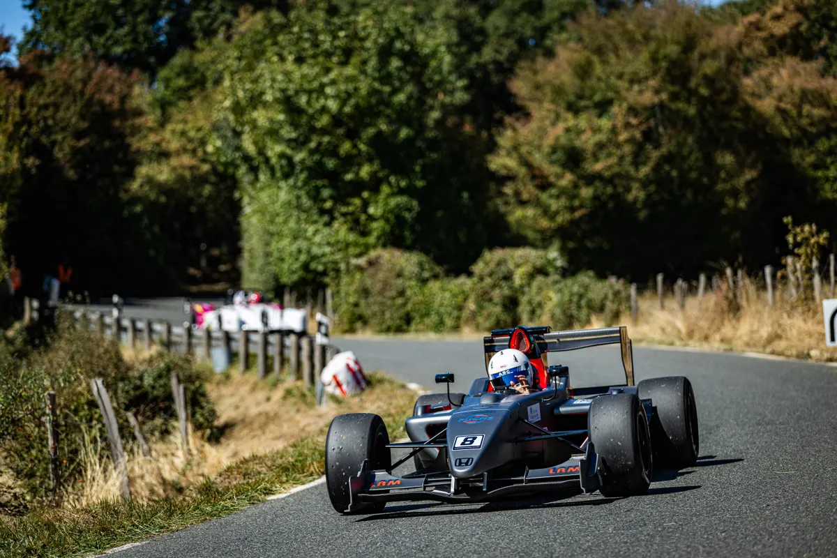 Monoplace noire avec casque blanc numérotée 8 en montée sur route sinueuse