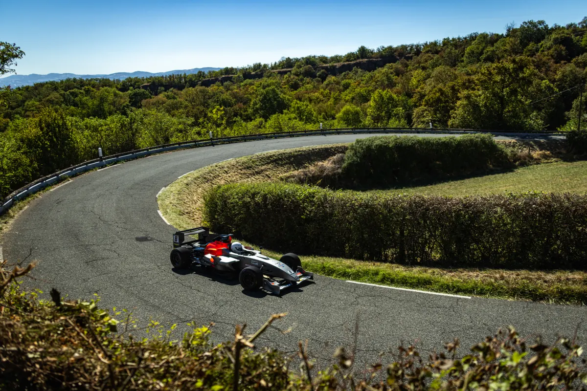 Monoplace noire et rouge dans un virage avec végétation autour